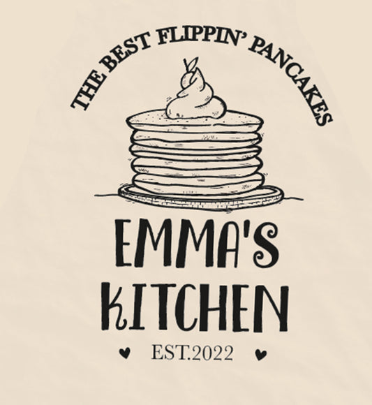Close Up of Pancake Day Apron. Text is The Best Kitchen Flippin' Pankcakes. Emma's Kitchen. Illustration of Pankcake with Cream.